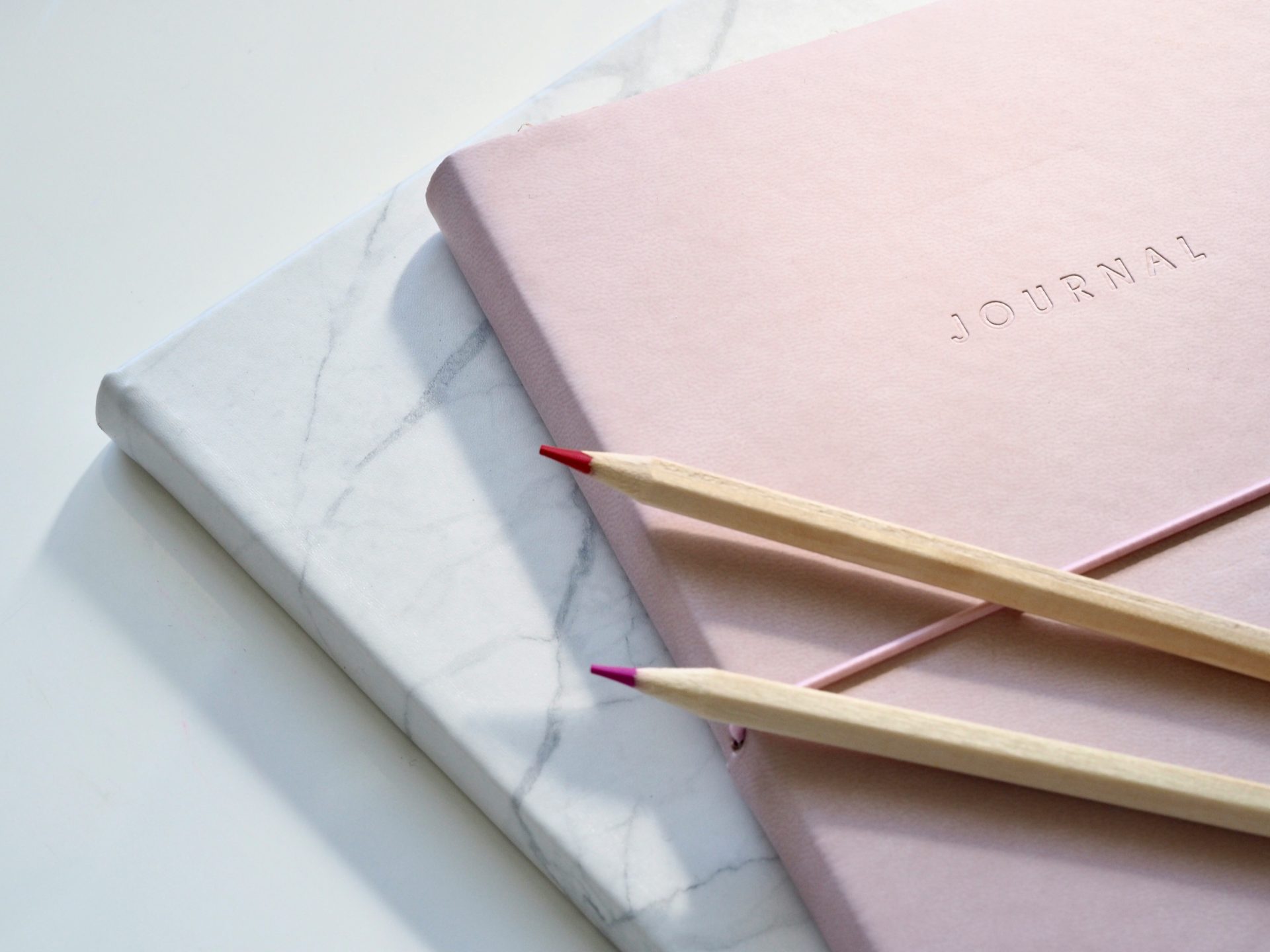 pink journal, pencils, white table